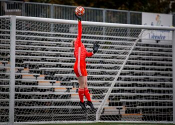 The soccer goalkeeper jumps up and tips the football over the crossbar of the soccer goals.