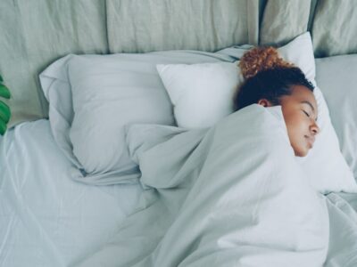 Young African American woman is sleeping in comfortable bed under warm blanket having rest on beautiful linen. Comfort, resting people and bedroom concept.