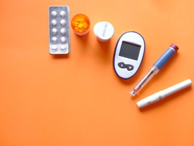 insulin pen, diabetic measurement tools and pills on orange background
